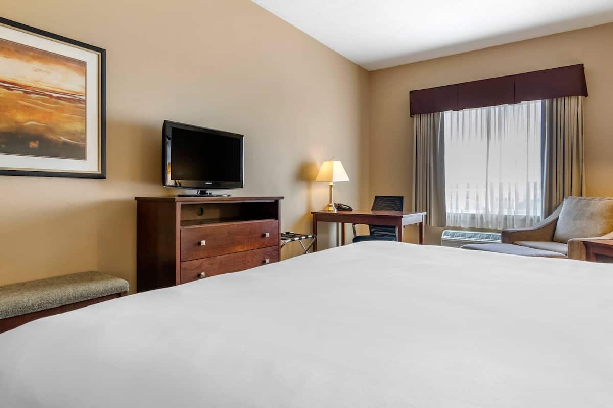 A hotel room with a large bed, a desk with a lamp, a television, and a chair.
