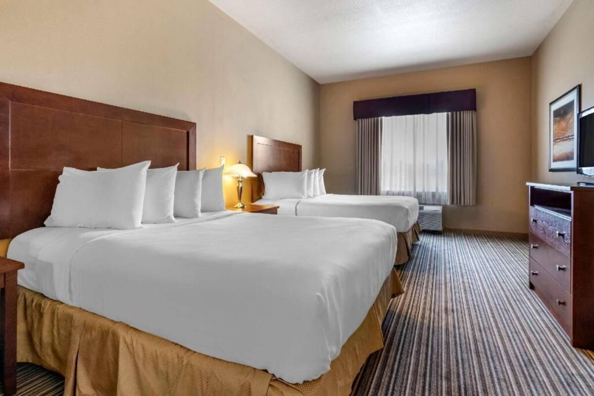 A hotel room with two beds, a TV, a desk, and a window with curtains.