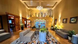 A spacious lobby with a high ceiling, a chandelier, and a patterned rug. There are several sofas and potted plants arranged for seating. - Quality Inn & Suites Rimbey (Rimbey)