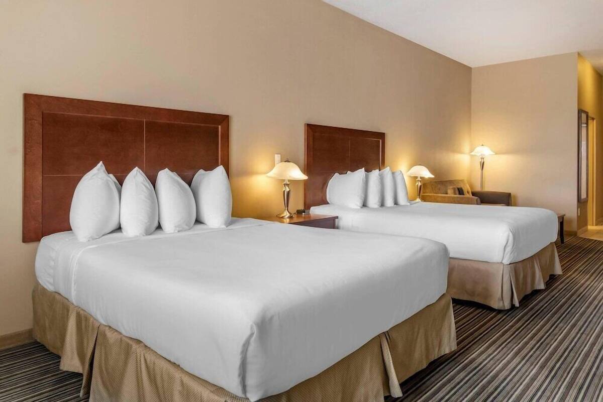 A hotel room with two beds, each with white linens and headboards, a small bedside table with a lamp, and a carpeted floor.