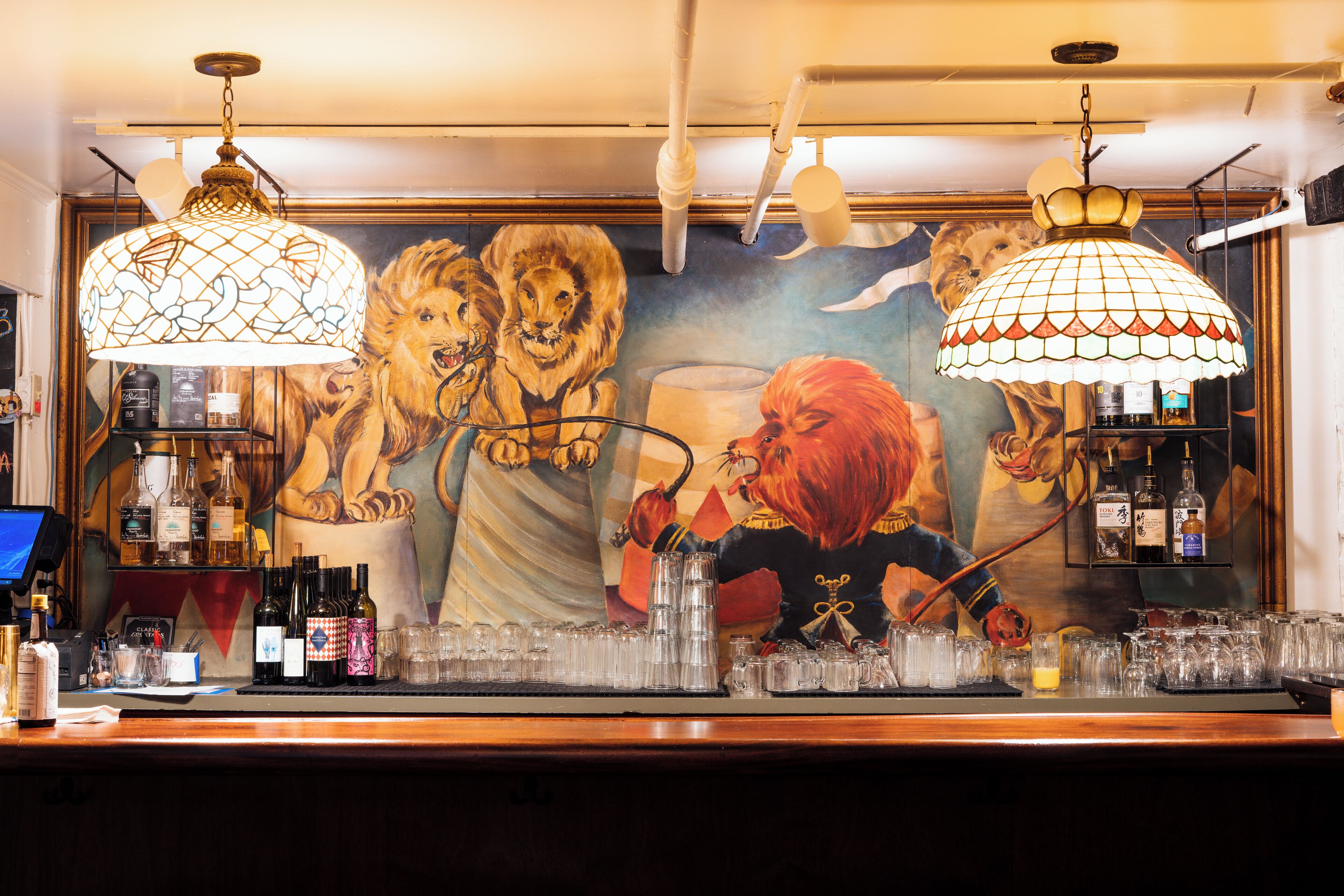 A bar area with a mural of lions, a variety of bottles, and glasses on the counter.