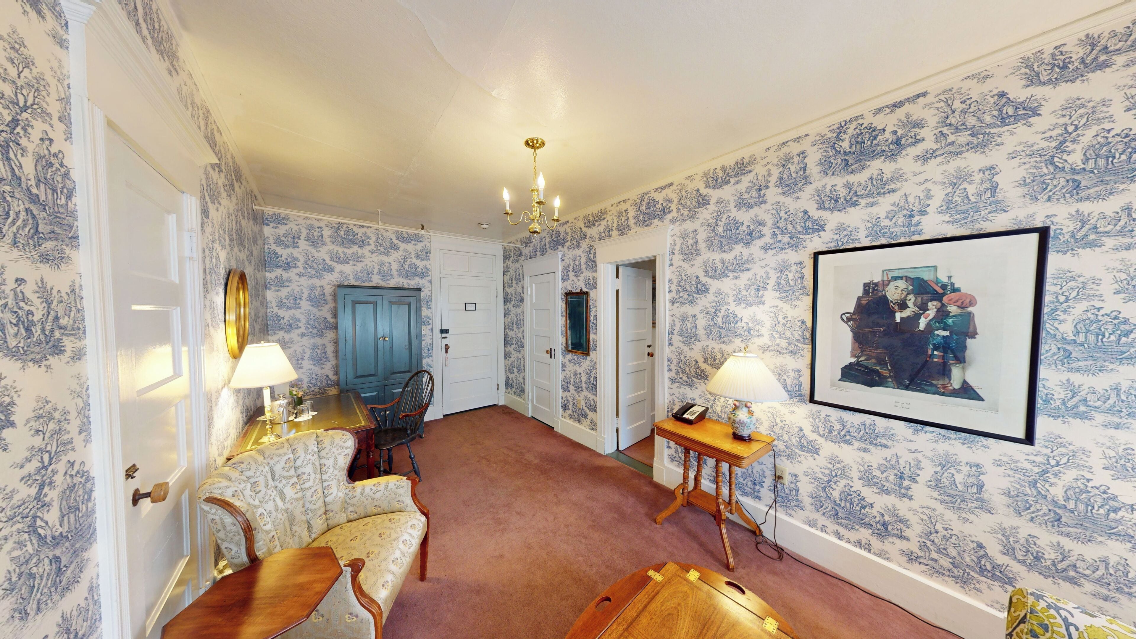 A hallway with patterned wallpaper, a chandelier, and a framed picture on the wall.