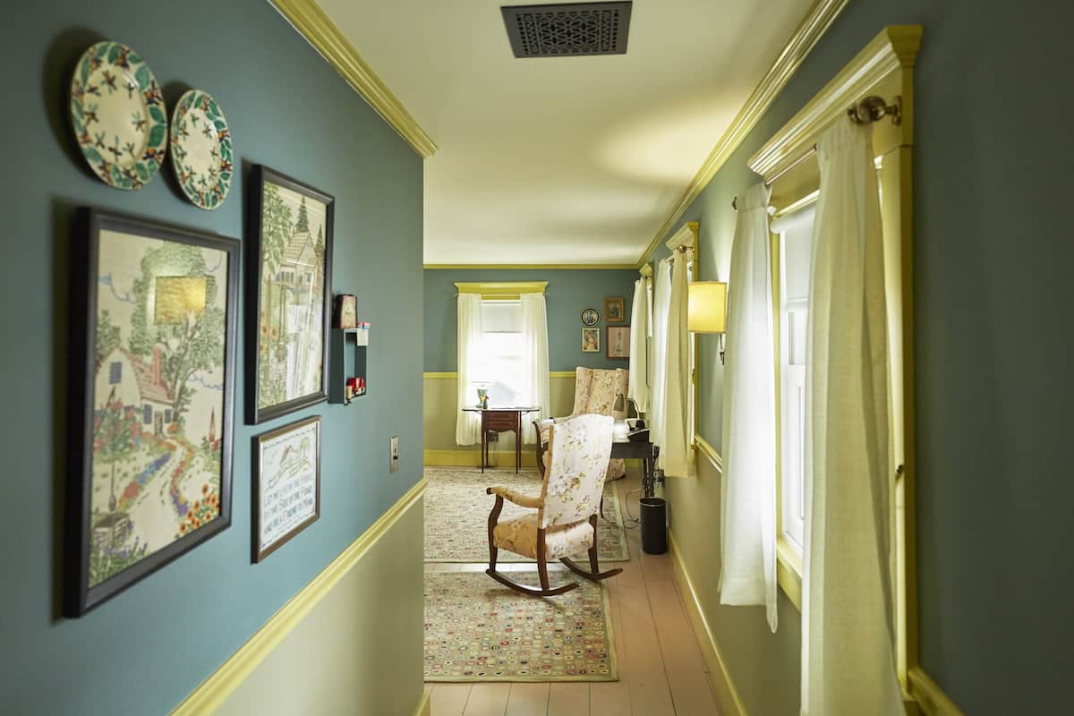A hallway with framed artwork, a rocking chair, and a dining area with a table and chairs.