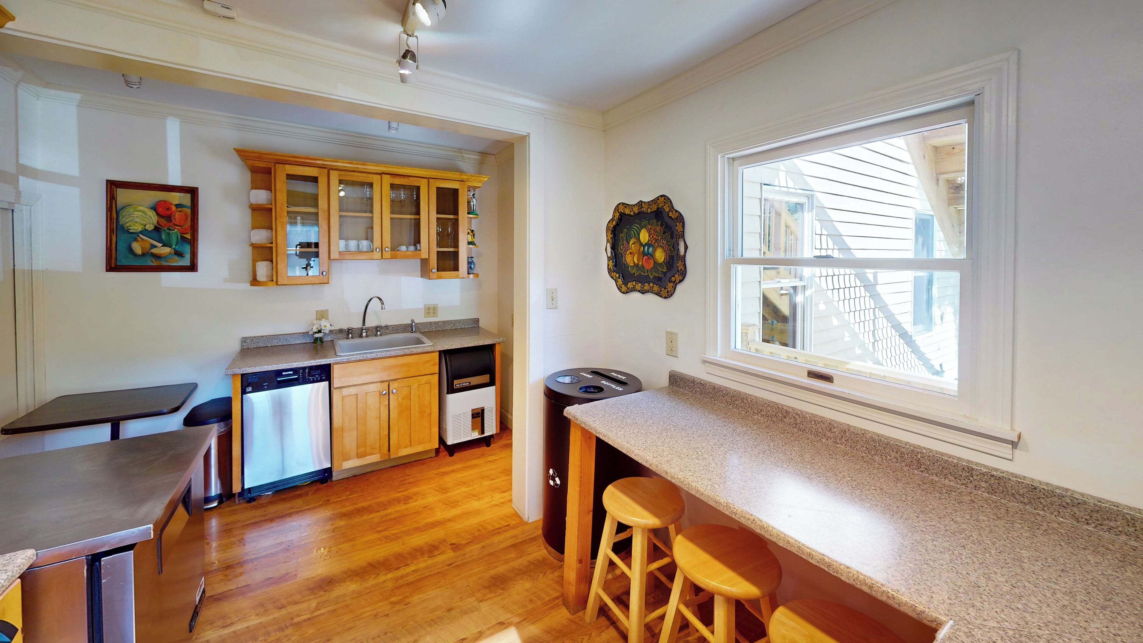 A kitchen with wooden cabinets, a dishwasher, a sink, and a window with a view of a house.