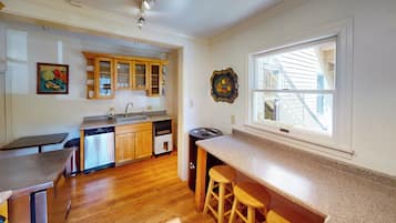 A kitchen with wooden cabinets, a dishwasher, a sink, and a window with a view of a house.