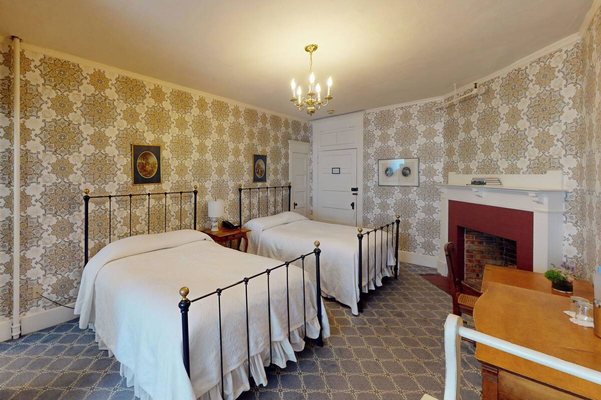 A room with two beds, a fireplace, and patterned wallpaper.