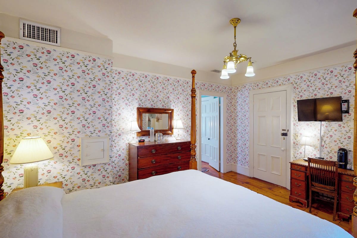 A bedroom with a four-poster bed, wooden dresser, and a television mounted on the wall.
