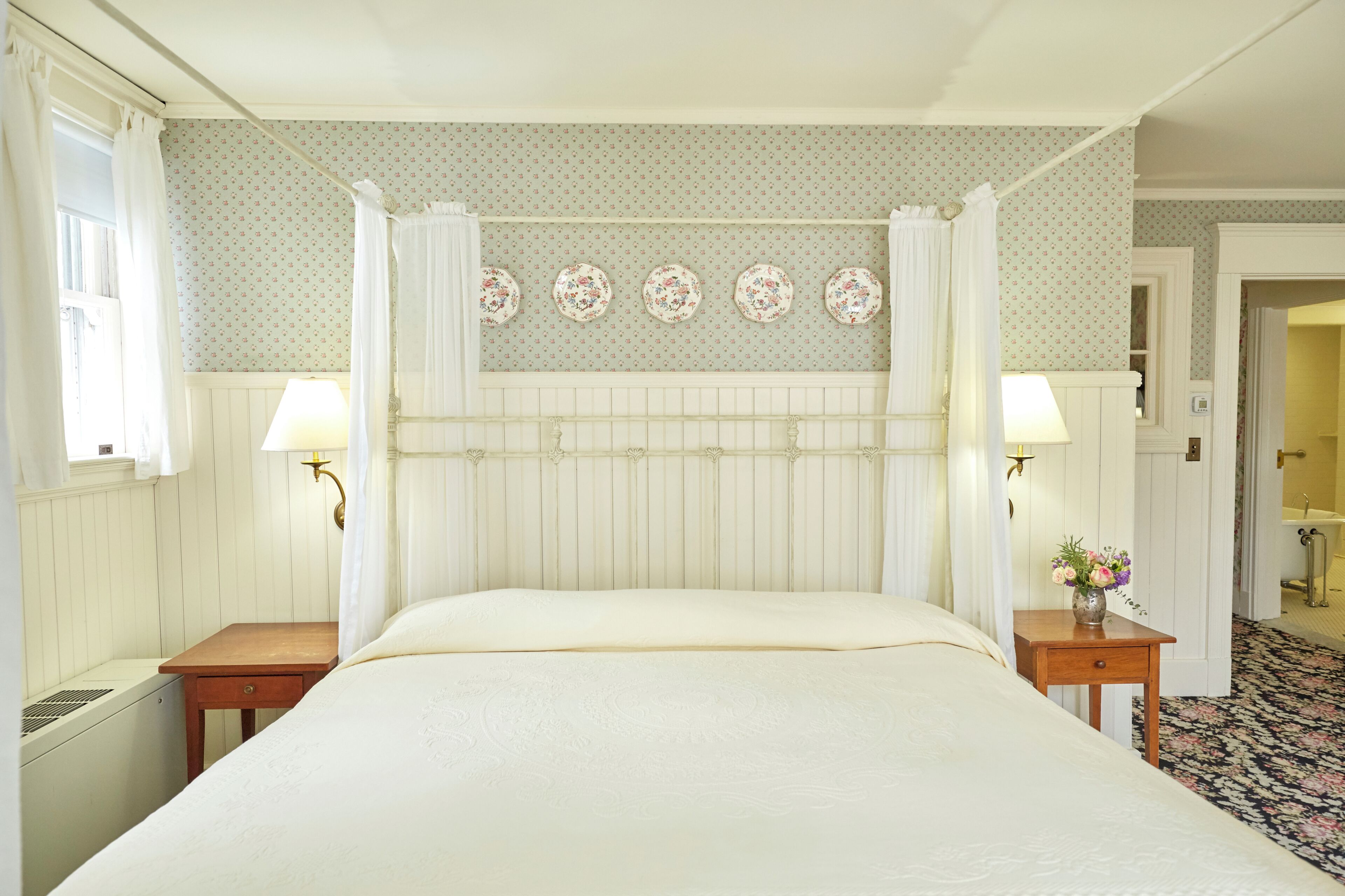 A neatly arranged bedroom with a bed, bedside tables, a wall-mounted lamp, and a floral-patterned wall.