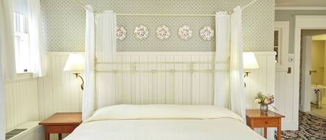 Une chambre à coucher bien rangée, avec un lit, des tables de chevet, une lampe fixée au mur et un papier peint à motifs floraux.