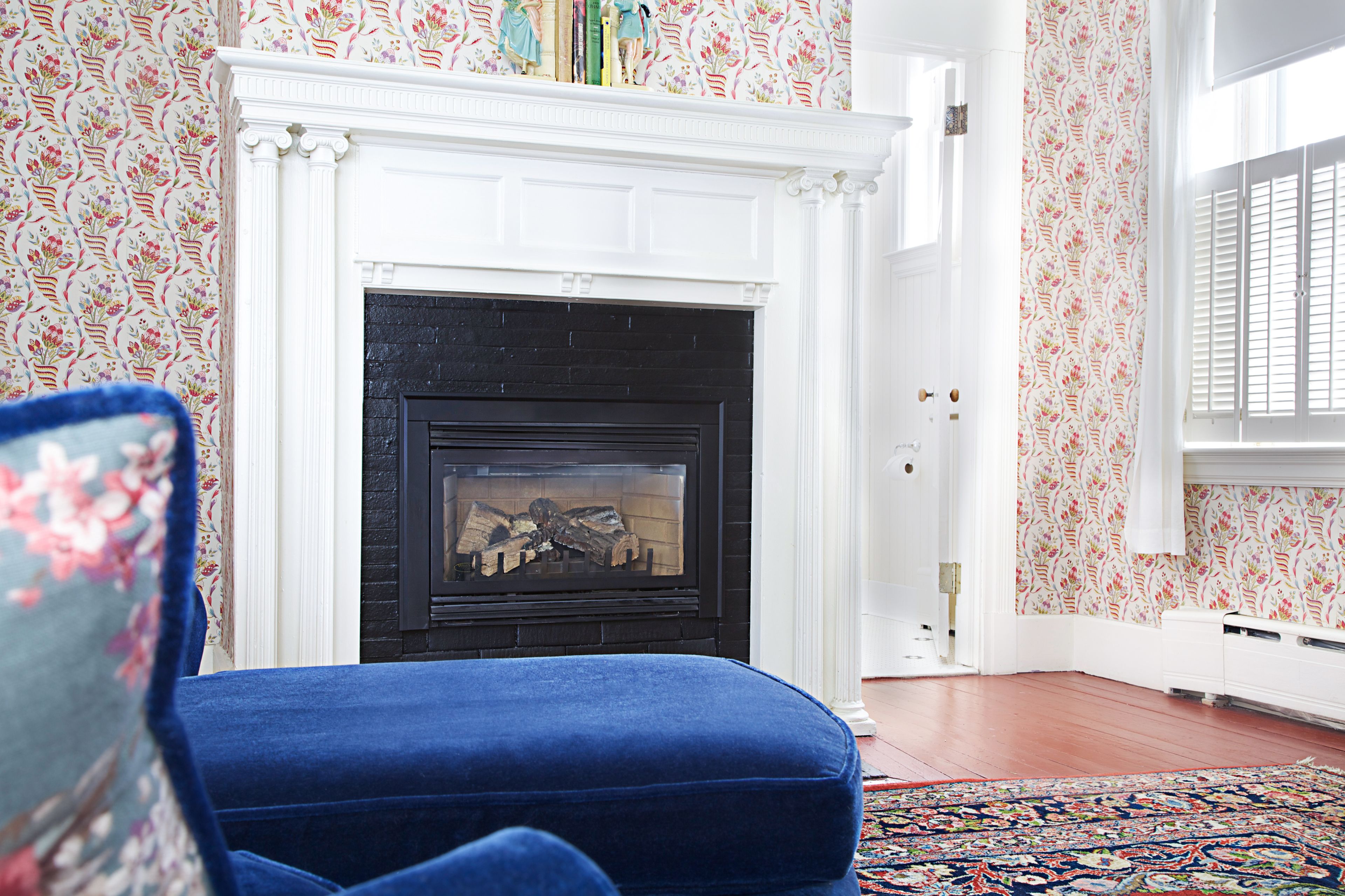 A room with a fireplace, floral wallpaper, and a blue upholstered chair.