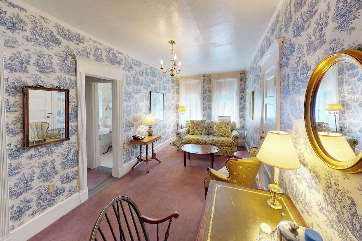 A room with patterned wallpaper, a chandelier, a sofa, a table, and a mirror.