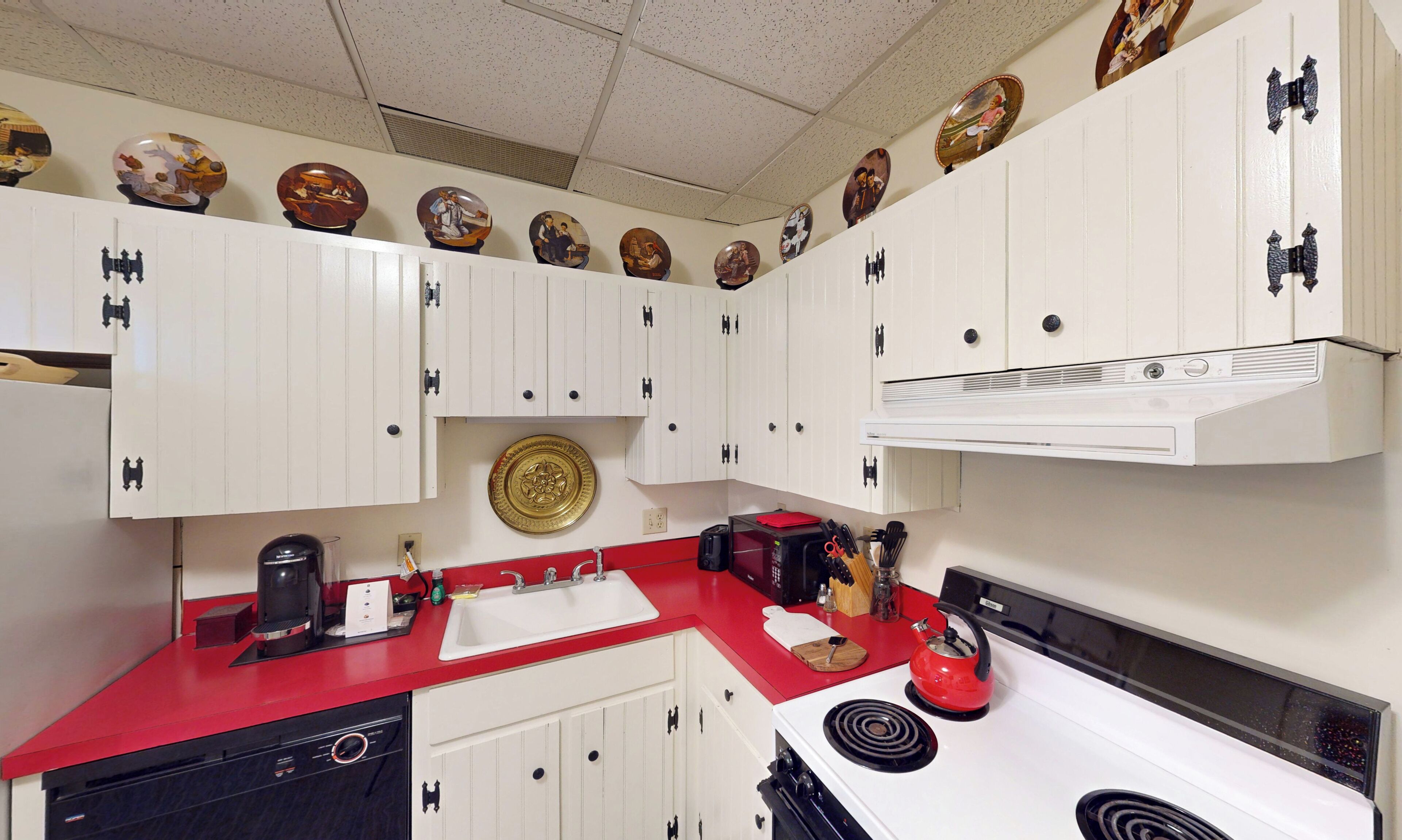A kitchen with white cabinets, a red countertop, a stove, and a microwave.