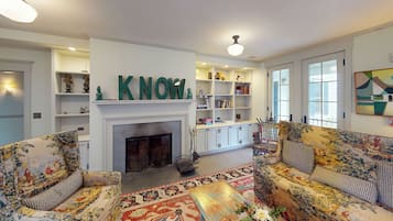 A living room with floral-patterned sofas, a fireplace, and a bookshelf with decorative items.