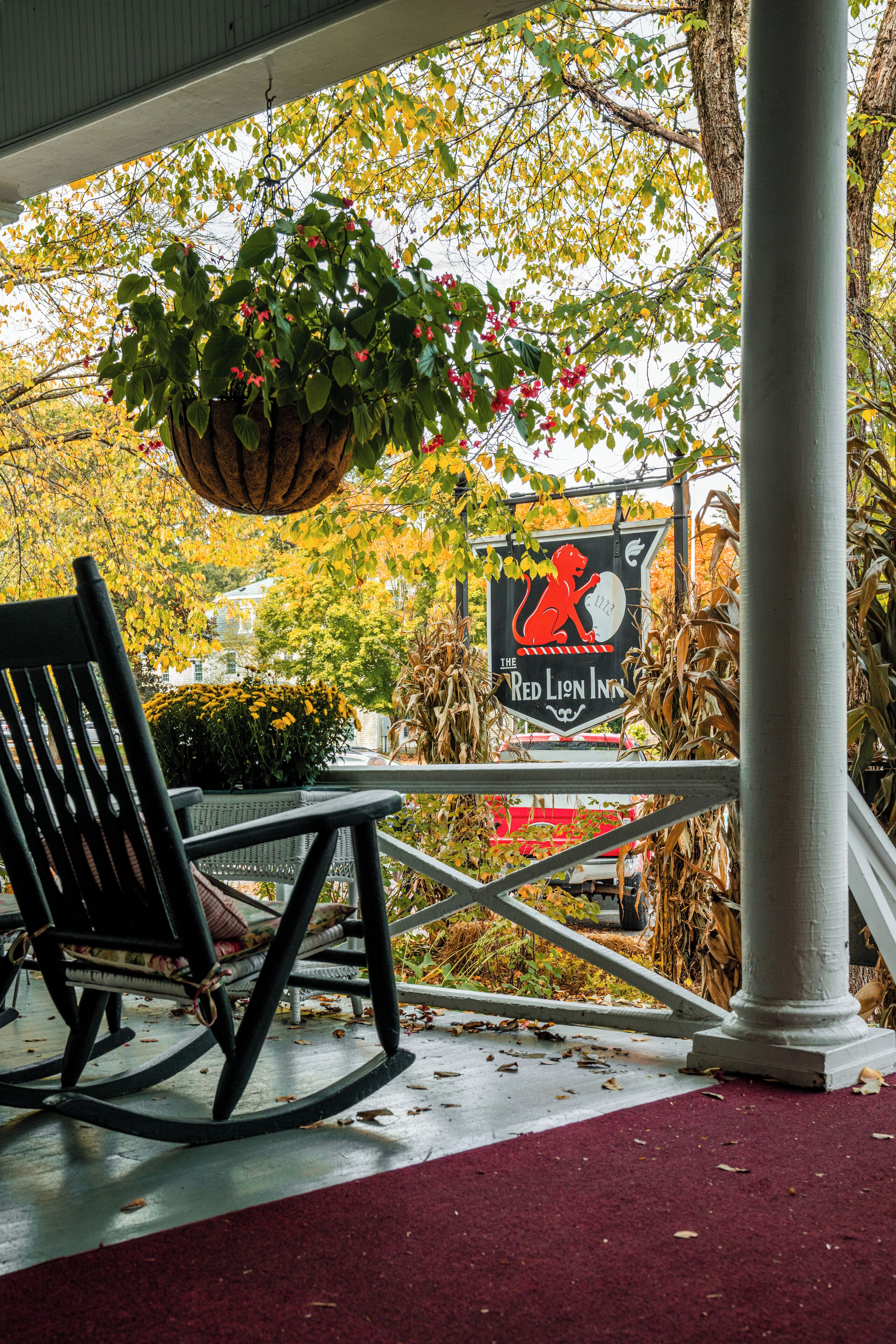 A rocking chair on a porch with a hanging plant and a sign for The Red Lion Inn.