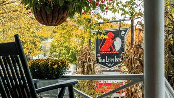A rocking chair on a porch with a hanging plant and a sign for The Red Lion Inn.