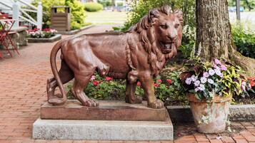 A lion statue on a pedestal in a garden area with a building in the background.