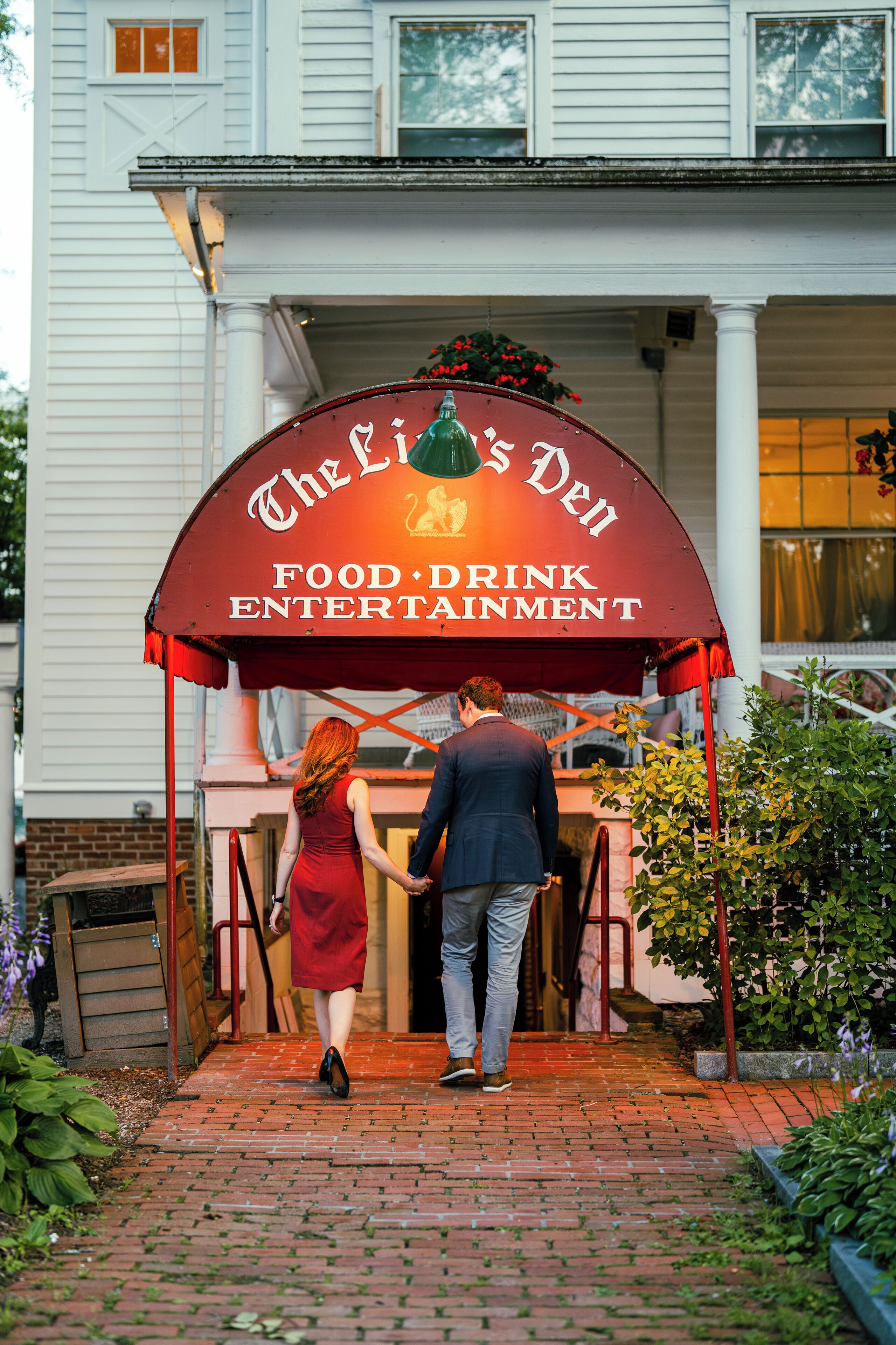 Un couple se dirige vers un bâtiment sur lequel est apposée une enseigne indiquant : « The Fish Den, restaurant, bar et lieu de divertissement ».