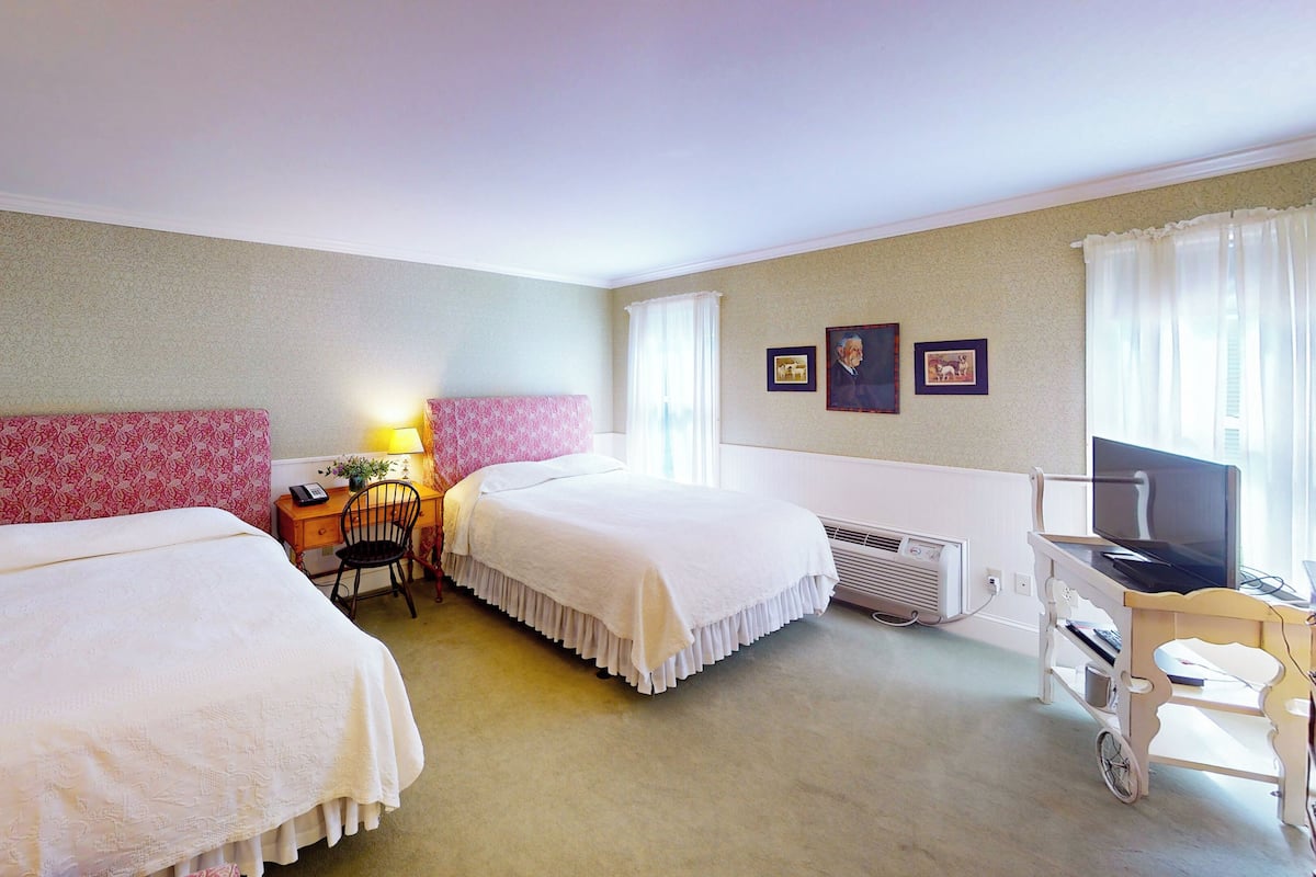 A hotel room with two beds, a desk with a chair, a television, and a radiator.