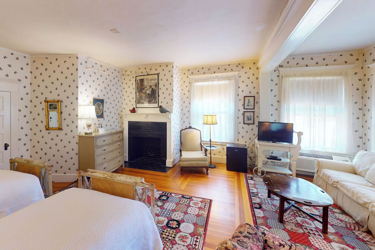 A hotel room with two beds, a fireplace, a television, and a sofa.