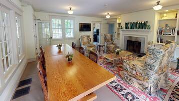 A spacious dining area with a wooden table and floral-patterned chairs, a fireplace, and a bookshelf with decorative items.