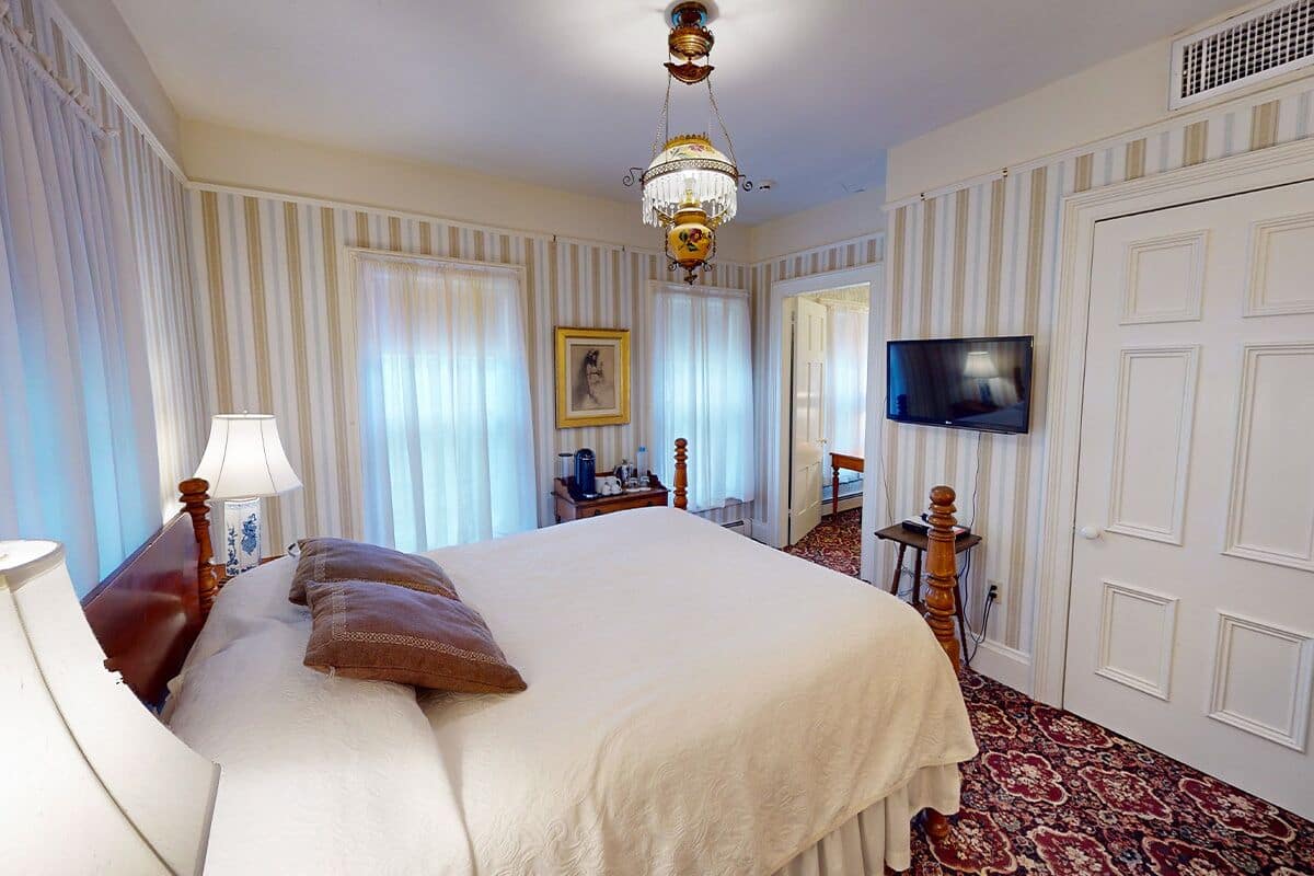 A hotel room with a large bed, a television, a chandelier, and a patterned carpet.