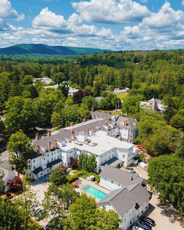 A large, multi-story building with a swimming pool, surrounded by dense greenery and trees.