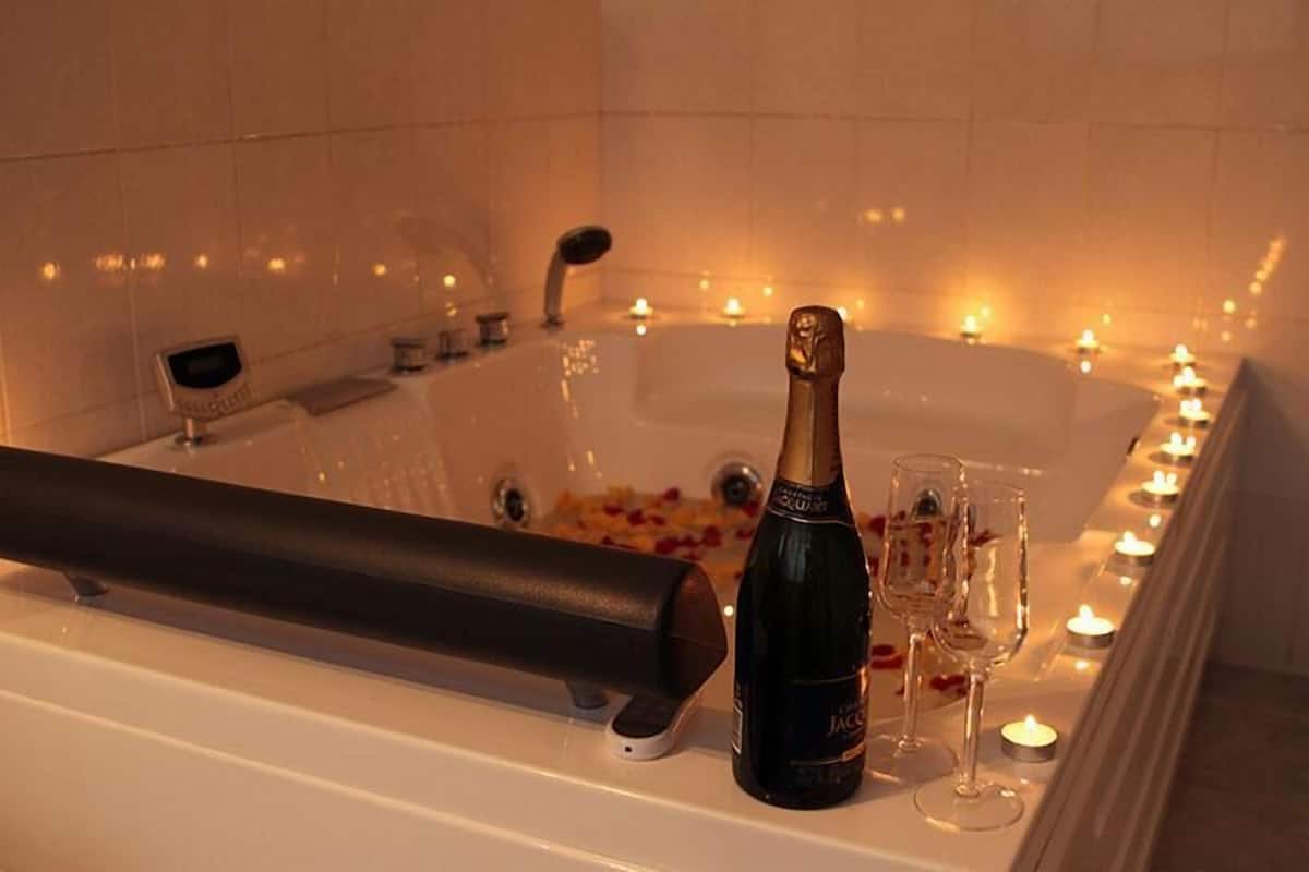 A bathtub with rose petals, a bottle of champagne, and glasses on a tray.