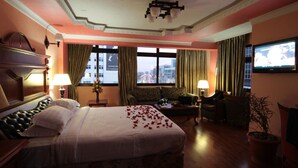 A hotel room with a large bed, a sofa, a television, and a view of the city through the windows. - Haimi Apartment Hotel (Addis Ababa)