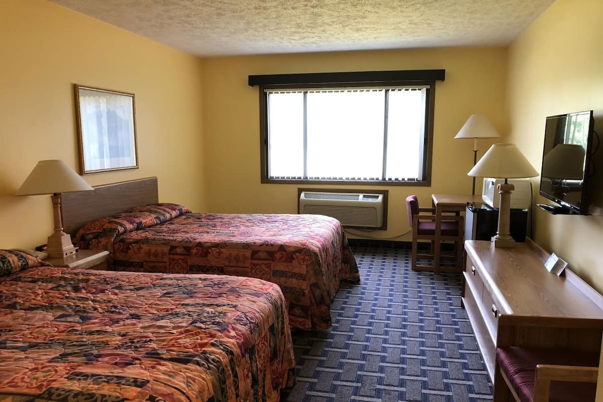 A hotel room with two beds, a desk, a TV, and a window with blinds.