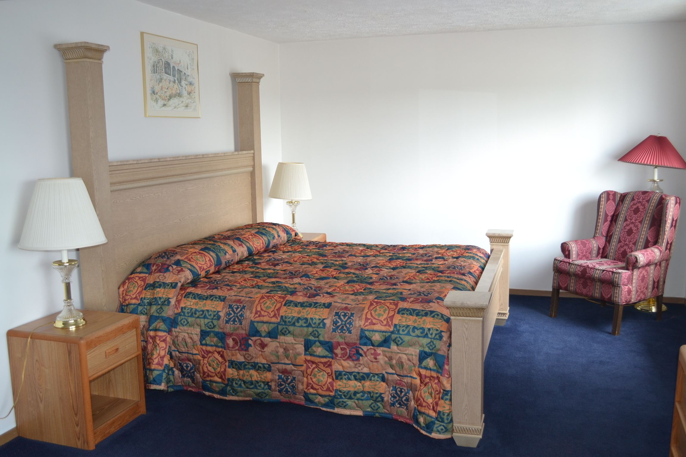 A hotel room with a bed, two bedside lamps, a chair, and a small wooden nightstand.