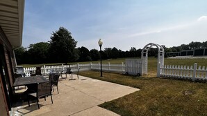 An outdoor patio with a table and chairs, a white picket fence, and a lawn. - Sky Lodge Inn & Suites (Delavan)