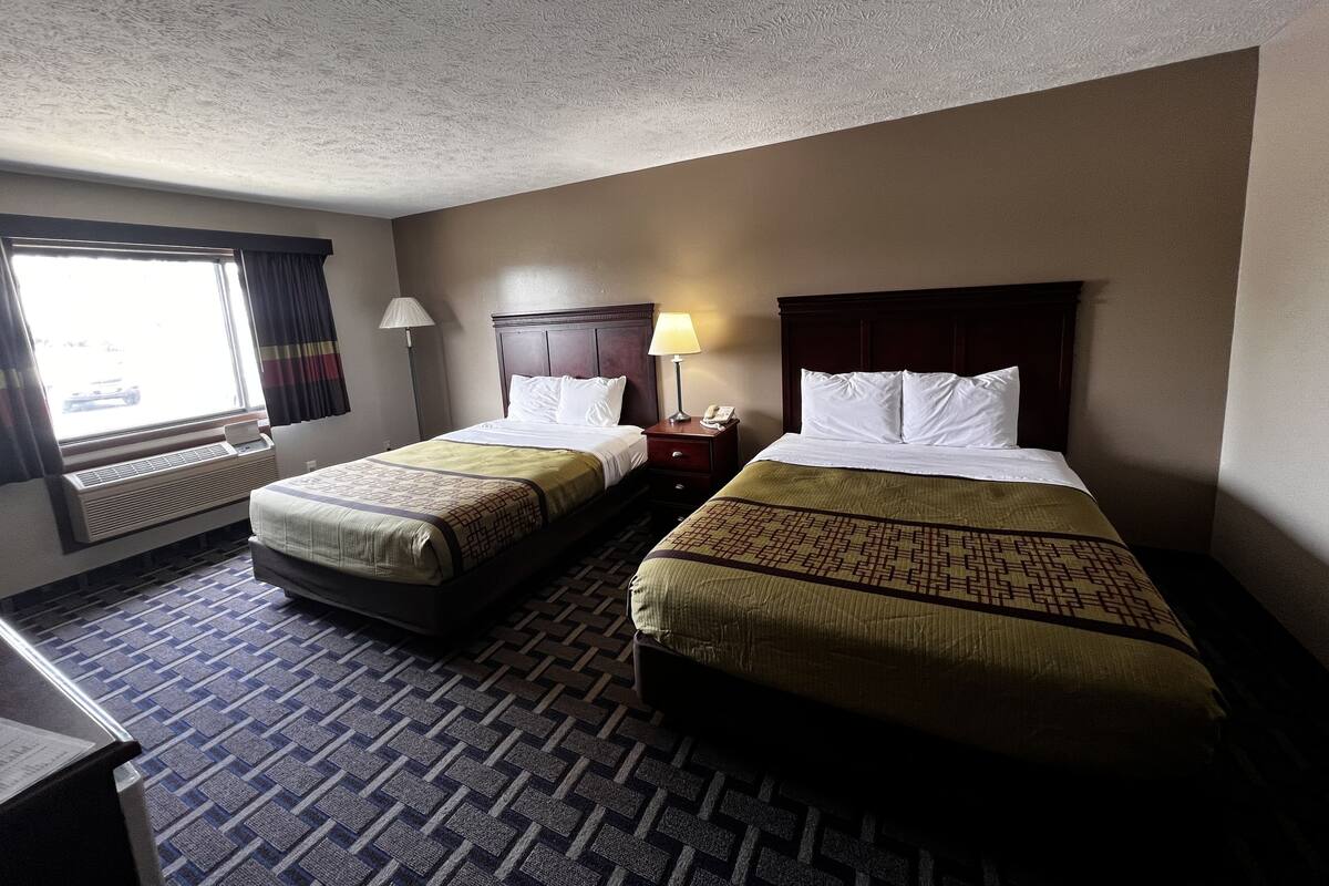 A hotel room with two beds, a desk, a chair, a window with curtains, and a radiator.