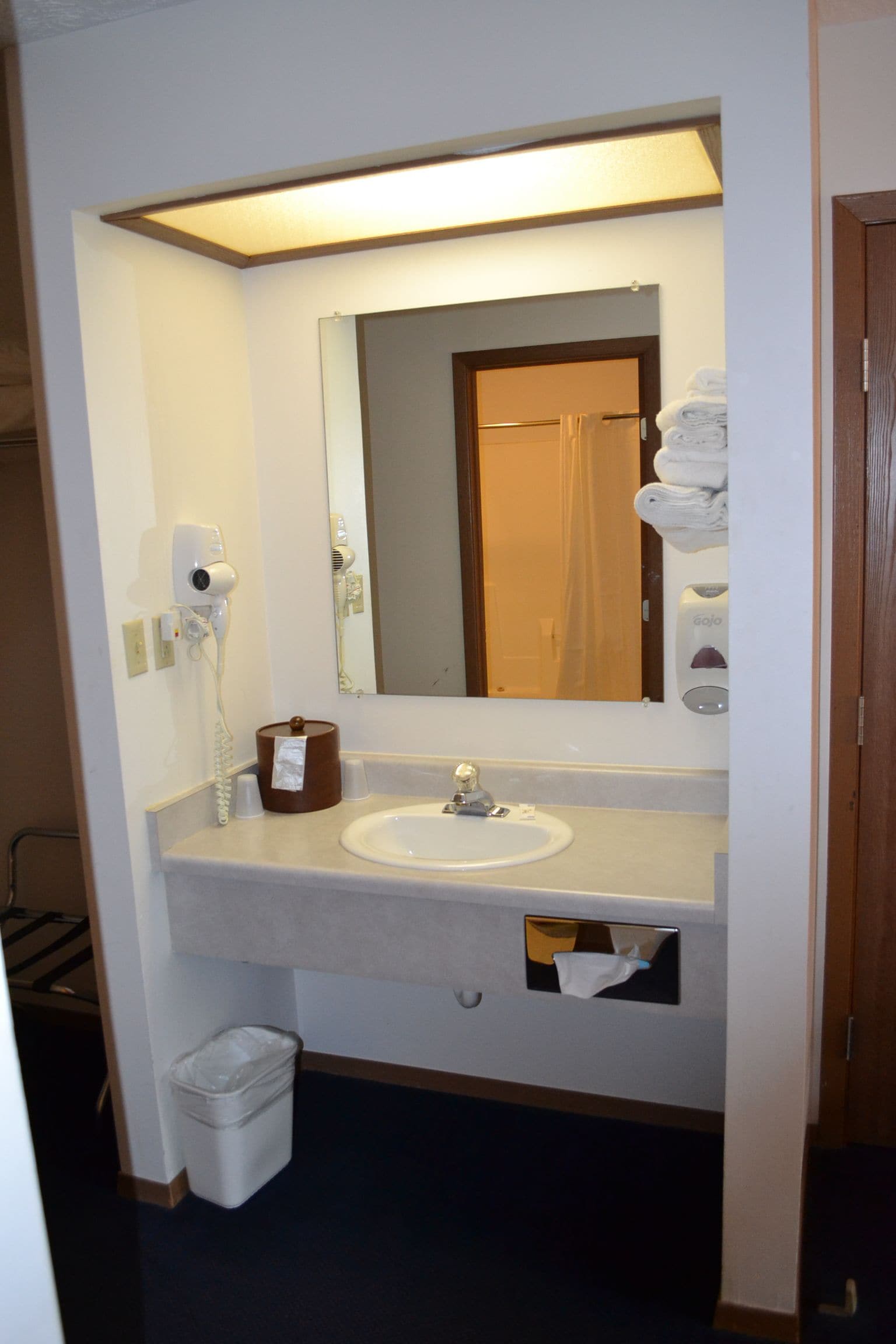 Casa de banho de hotel com lavatório, espelho, secador de cabelo e dispensador de toalhas.