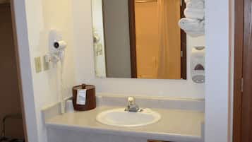 Un baño de hotel con lavamanos, espejo, secador de pelo y dispensador de toallas.