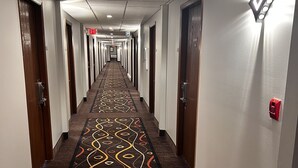 A hotel hallway with patterned carpet, doors, and emergency exit signs. - Sky Lodge Inn & Suites (Delavan)