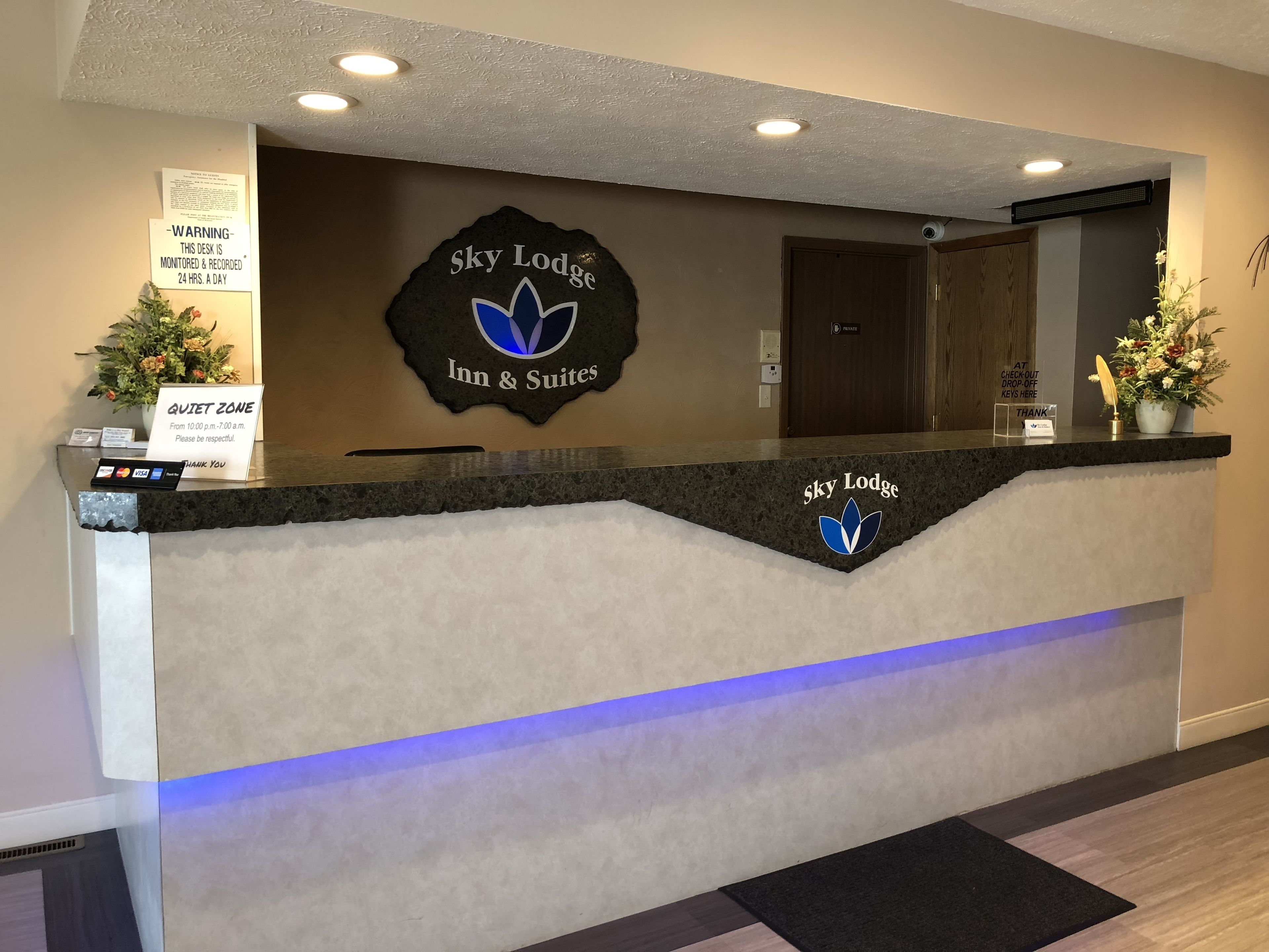 Un comptoir d’accueil à l’hôtel Sky Lodge Inn & Suites, avec un panneau indiquant une « zone de silence », une carte de remerciement et un panneau indiquant où déposer les clés au moment du départ (« Déposez vos clés ici pour le départ »).