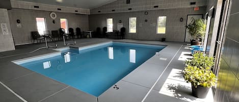 An indoor swimming pool with a tiled floor, chairs, and potted plants.