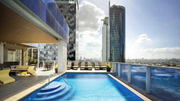 Une piscine sur le toit offrant une vue sur la ville, une architecture moderne et des espaces de détente en plein air.