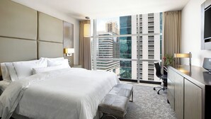 Une chambre d’hôtel moderne, dotée d’un grand lit, d’un bureau et offrant une vue sur le paysage urbain.