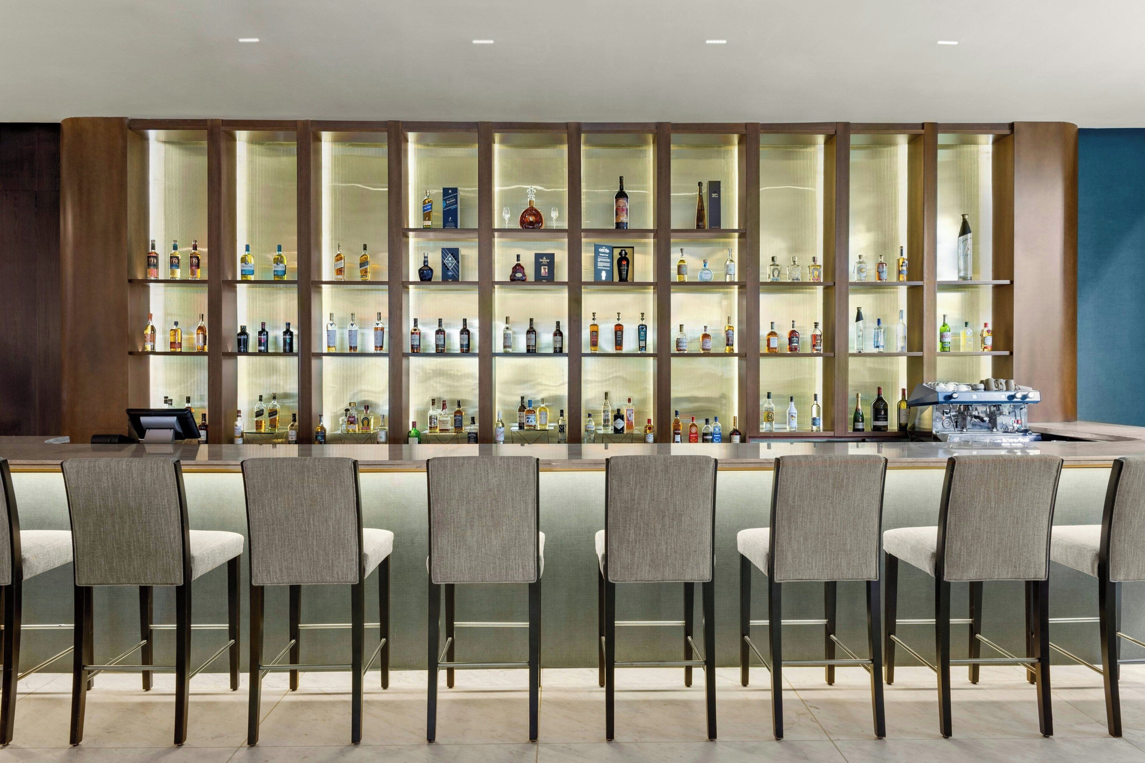 Zona de bar con varios estantes llenos de botellas de licor, taburetes y barra.