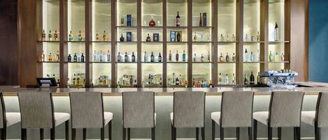 Zona de bar con varios estantes llenos de botellas de licor, taburetes y barra.