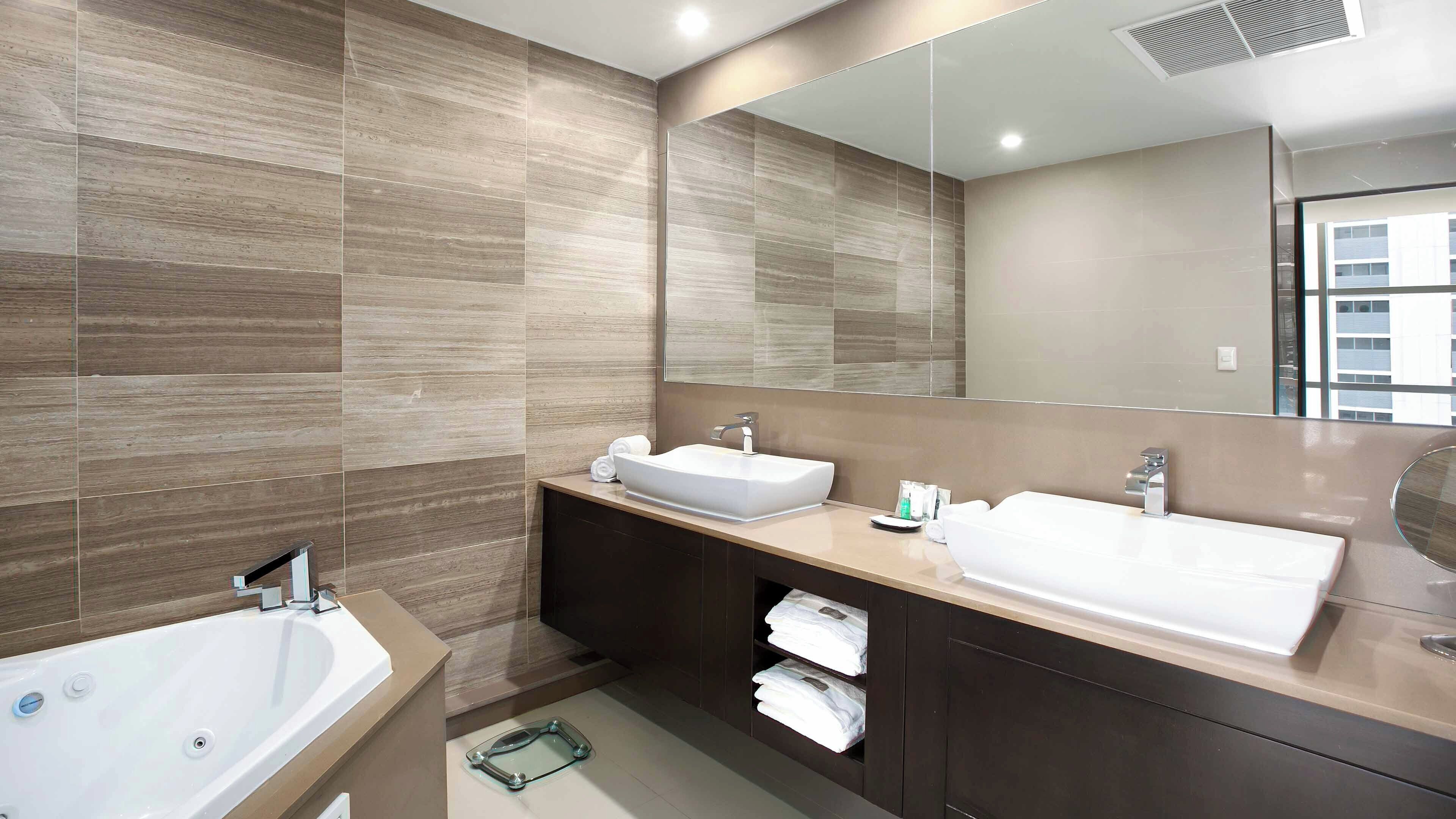 A modern bathroom with two sinks, a bathtub, and a large mirror.