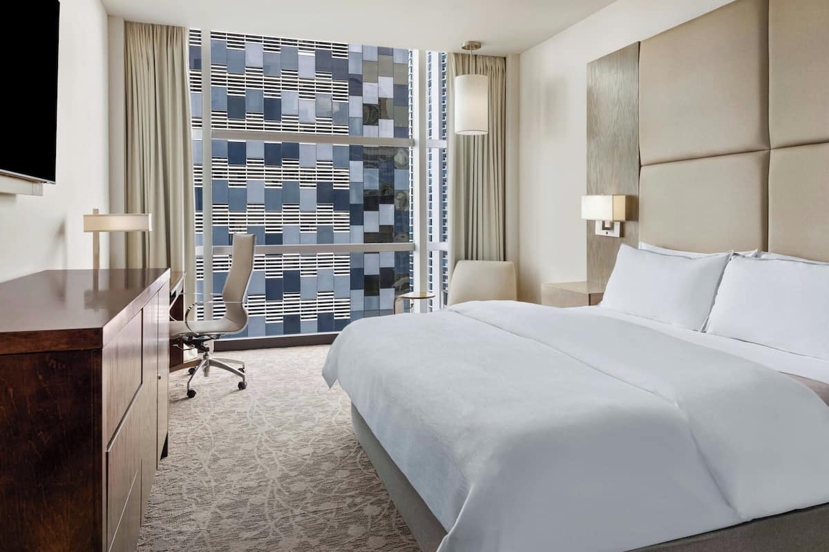 Une chambre d’hôtel avec un grand lit, un bureau avec une chaise, une télévision et une fenêtre ornée d’un motif géométrique.
