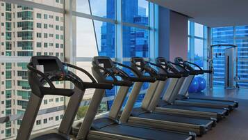 Un gimnasio con cintas de correr alineadas, ventanas amplias y vistas a un paisaje urbano.