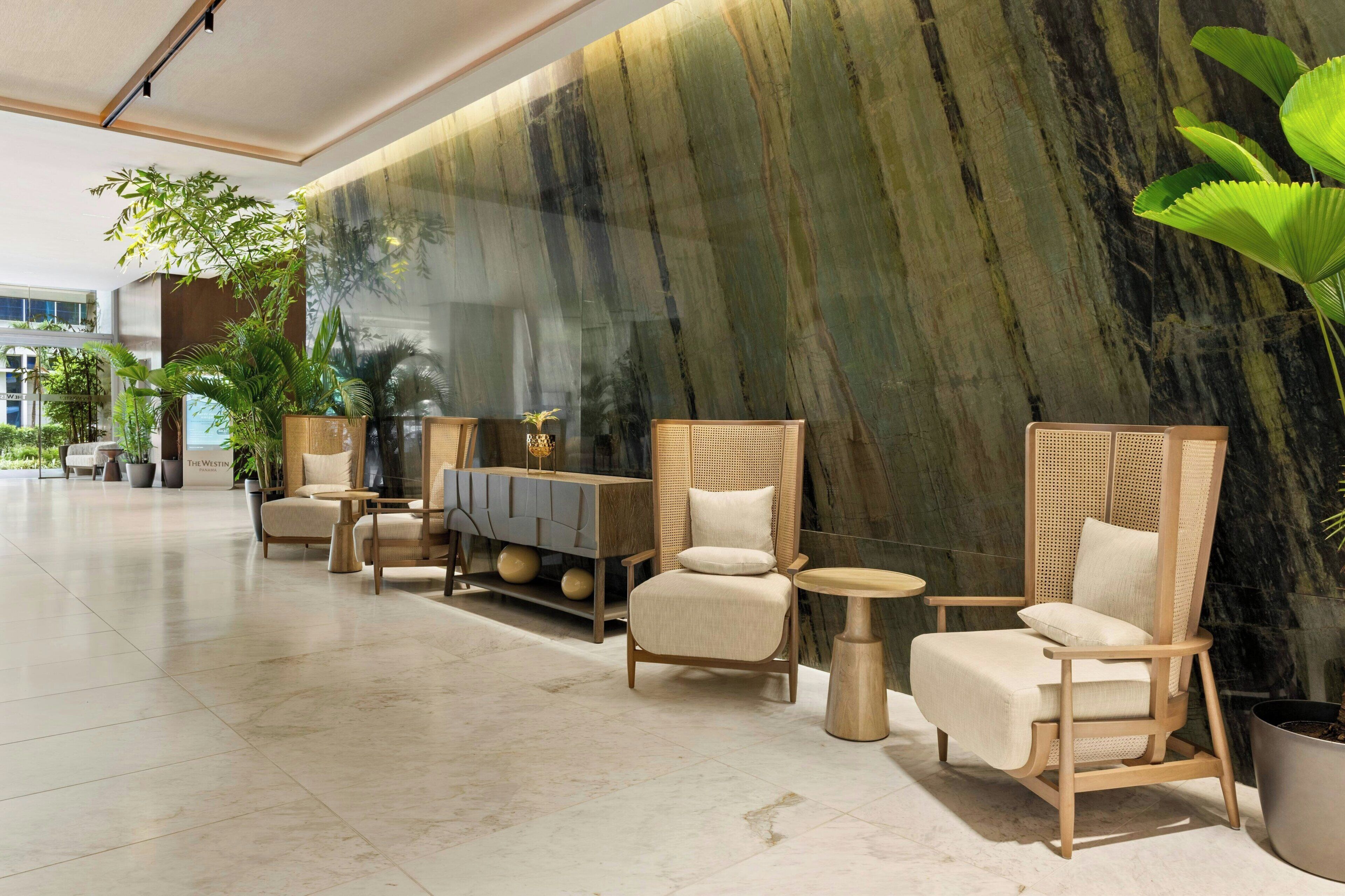 A lobby with seating arrangements, a marble wall, and potted plants.