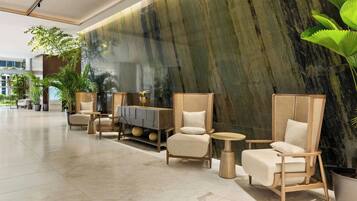 A lobby with seating arrangements, a marble wall, and potted plants.