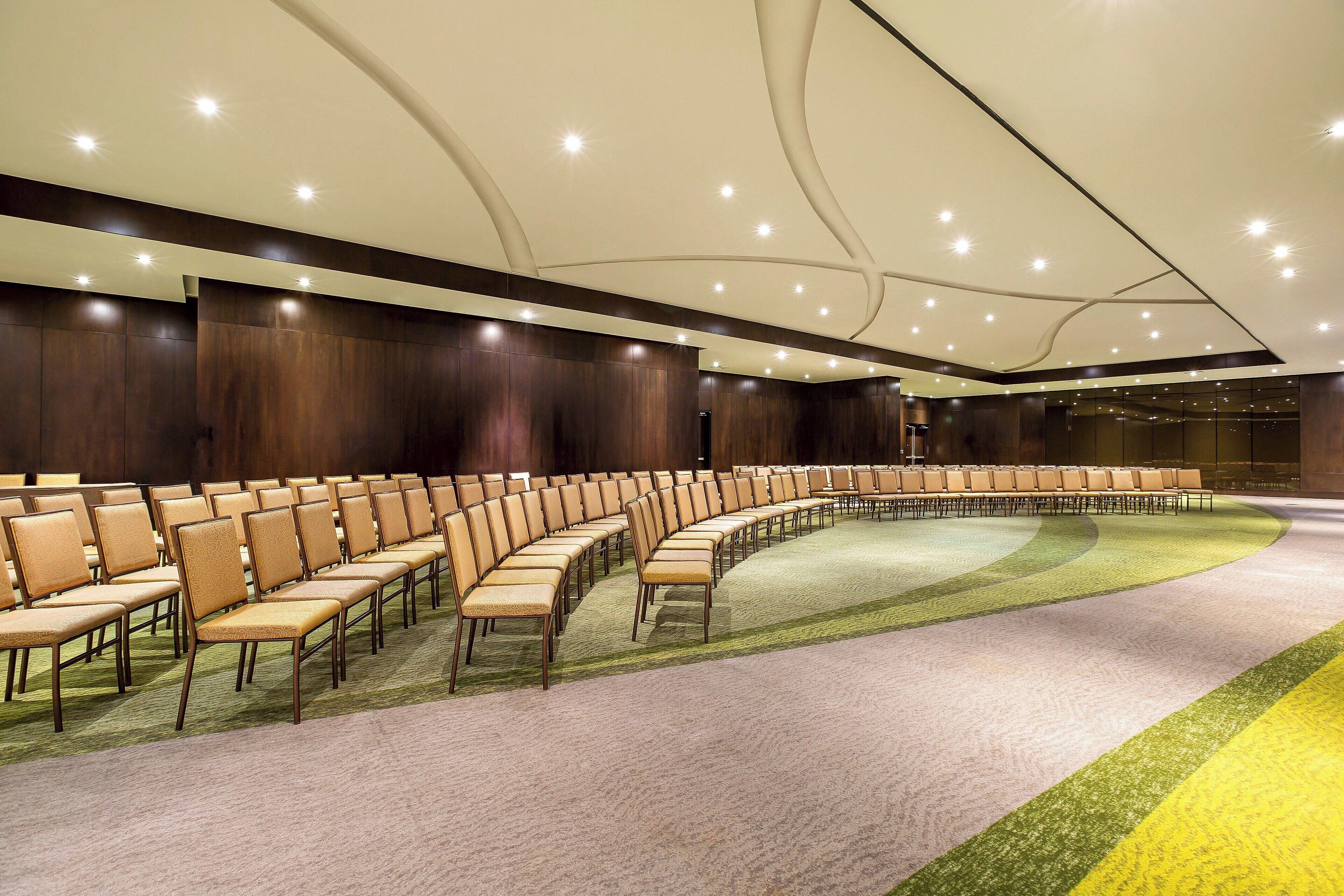 A conference room with rows of chairs, a carpeted floor, and a curved ceiling with recessed lighting.