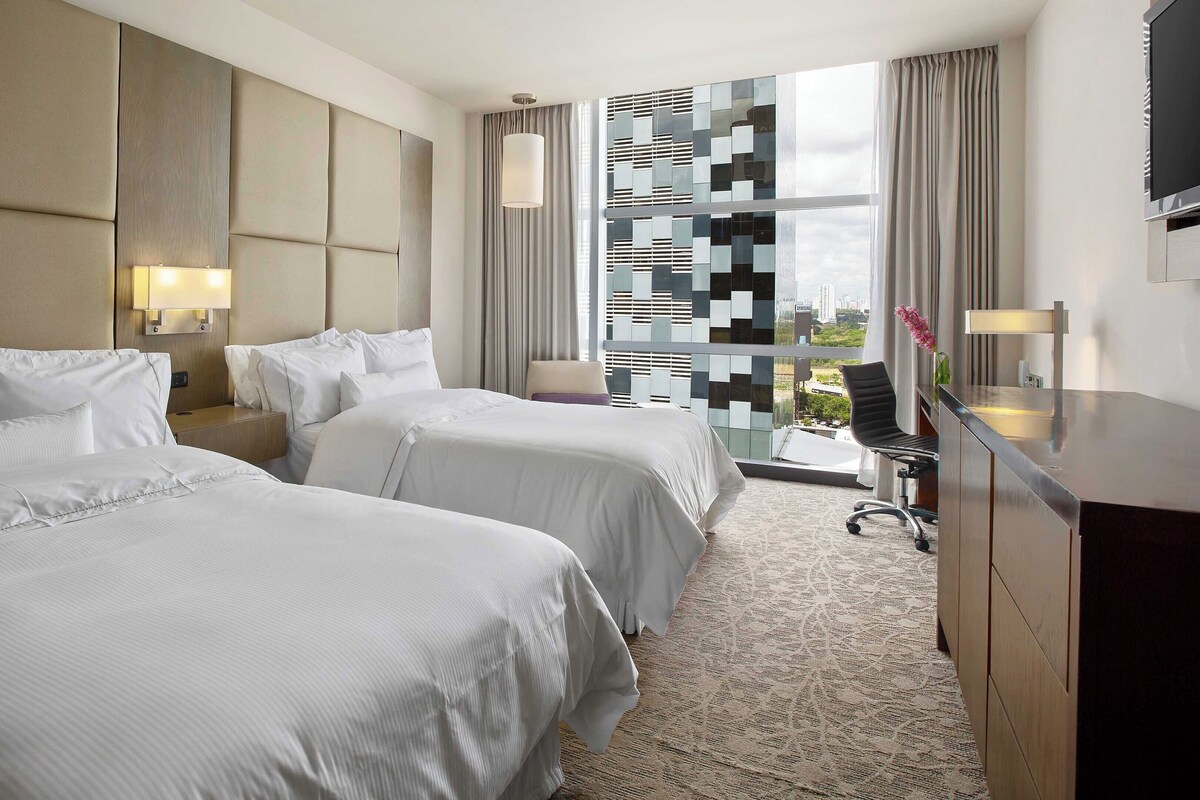 Ein Hotelzimmer mit zwei Betten, einem Schreibtisch und einem großen Fenster mit Blick.