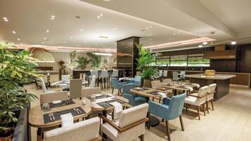 A modern restaurant with round tables, blue chairs, and potted plants.