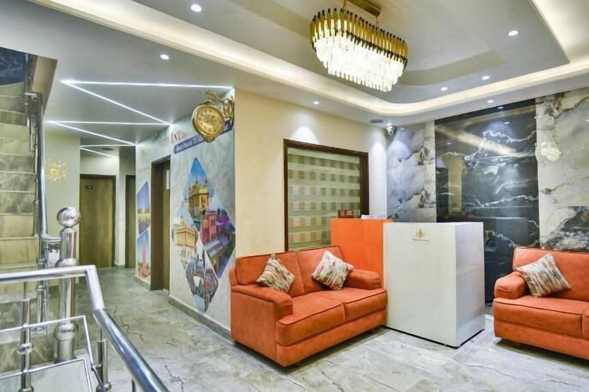 Un área de recepción con dos sofás naranjas, una araña de cristal, una pared de mármol y una escalera.